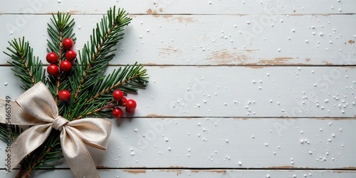 Festive evergreen branch with a satin ribbon bow and bright red berries on a rustic white wood background, ideal for holiday greetings or seasonal designs.