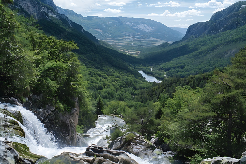 A stunning waterfall plunges down rocky cliffs, cascading into a lush green valley with a winding river. Mountains rise in the distance under a partly cloudy sky.