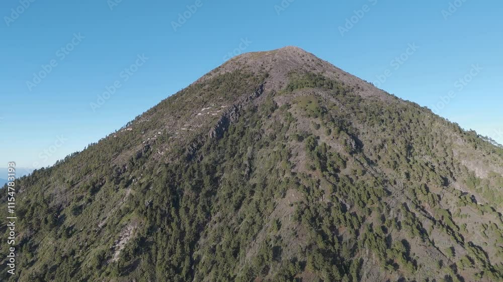 View of the steep, forested slopes of Volcan Acatenango leading up to its rocky summit, under a bright, clear blue sky View of the steep, forested slopes of Volcan Acatenango leading up to its rocky summit, under a bright, clear blue sky