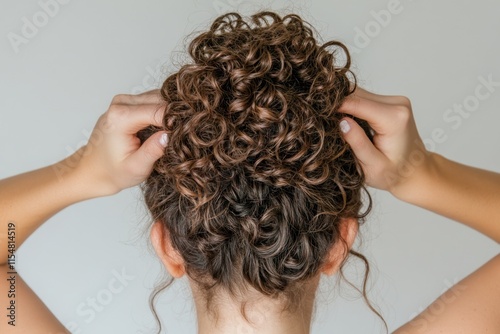 A woman tying her curly hair into a bun, with soft focus on her hands and hair texture under natural light