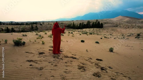 Monk in red robe raising hands toward the sky in desert landscape