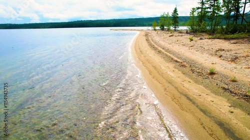 Aerial view of sandy shoreline meeting clear waters and forest