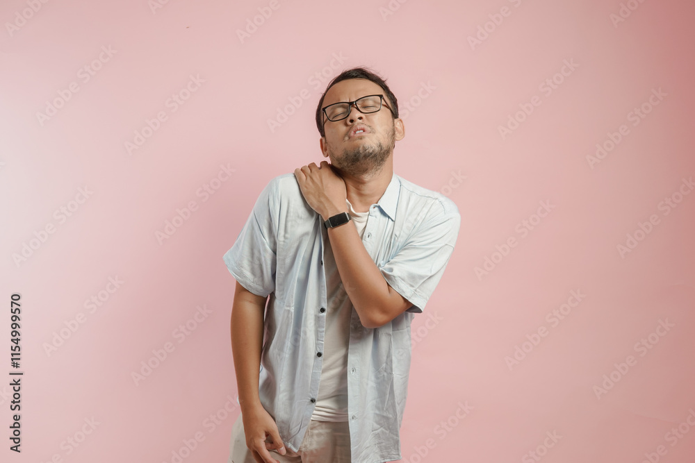 Tired young Asian man wearing shirt suffering from pain, muscle spasm on the shoulder and neck. Tired young Asian man wearing shirt suffering from pain, muscle spasm on the shoulder and neck.
