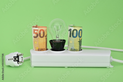 Euro money paper banknotes and turned off light bulb in unplugged white power strip sockets on the green background. Concept of saving money on electricity consumption.

 photo