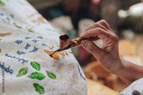 Close up picture of a person's hand drawing the design pattern of Indonesian batik tulis fabric.