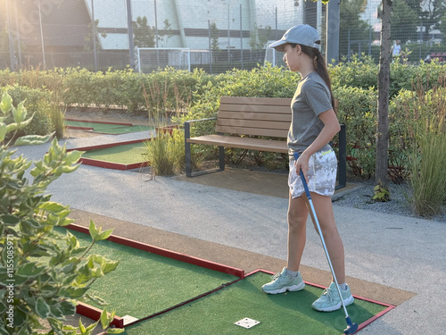 Little active child, cute toddler girl, playing miniature golf enjoying sunny summer vacation day outdoors in the park. photo