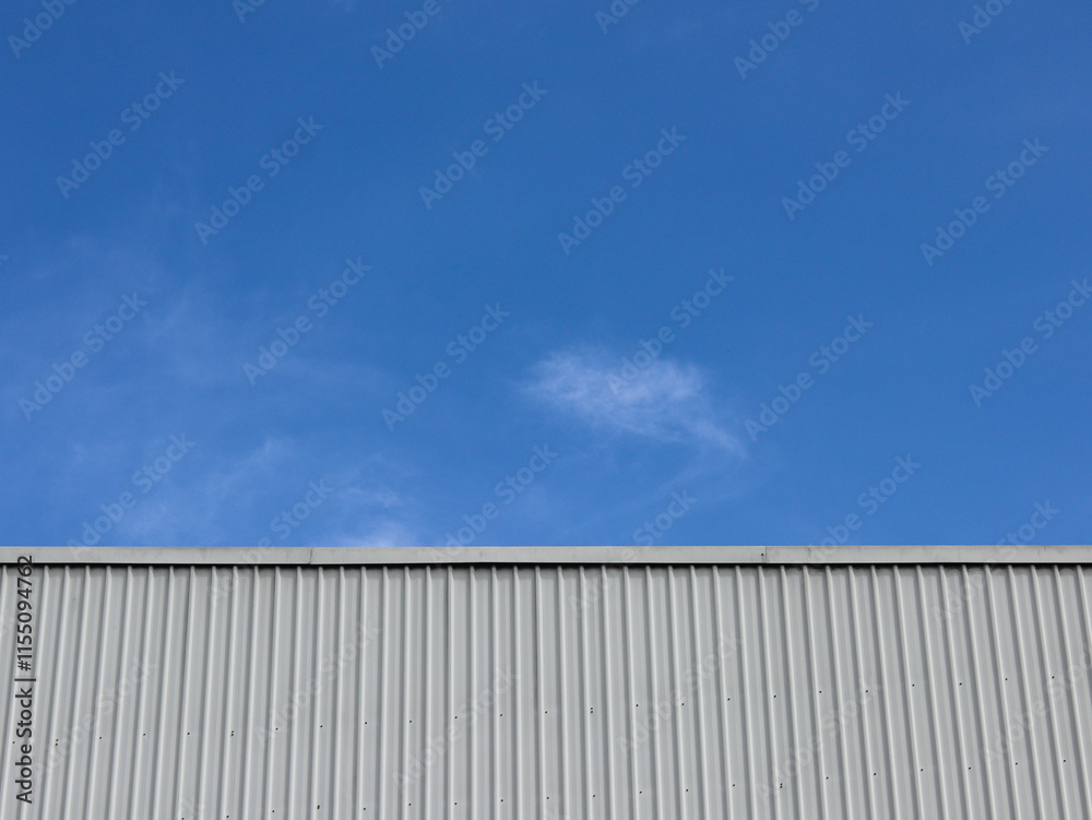Industrial factory building with aluminum metal texture on the exterior wall against the background of blue sky and clouds, modern architecture of corrugated steel facade. Copyspace, design. Industrial factory building with aluminum metal texture on the exterior wall against the background of blue sky and clouds, modern architecture of corrugated steel facade. Copyspace, design.