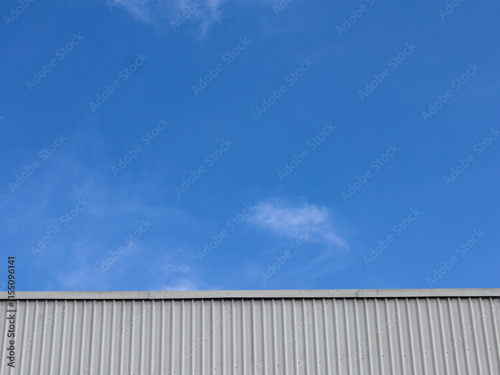 Industrial factory building with aluminum metal texture on the exterior wall against the background of blue sky and clouds, modern architecture of corrugated steel facade. Copyspace, design. Industrial factory building with aluminum metal texture on the exterior wall against the background of blue sky and clouds, modern architecture of corrugated steel facade. Copyspace, design.