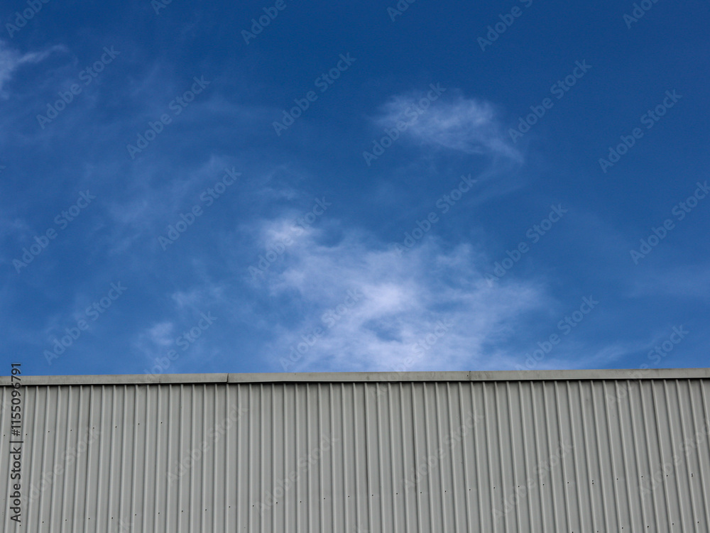 Industrial factory building with aluminum metal texture on the exterior wall against the background of blue sky and clouds, modern architecture of corrugated steel facade. Copyspace, design. Industrial factory building with aluminum metal texture on the exterior wall against the background of blue sky and clouds, modern architecture of corrugated steel facade. Copyspace, design.
