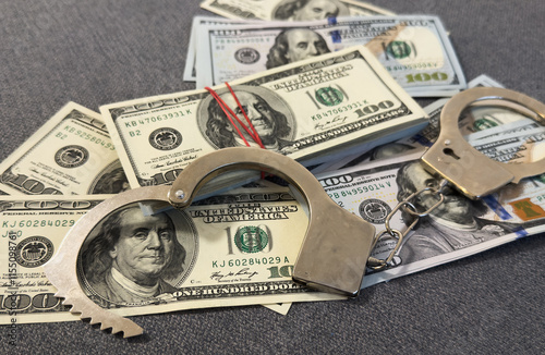 Financial crime, fraud, money laundering, corruption, or law enforcement : Bundles of US dollar 100 bills in a small case, alongside a pair of handcuffs placed over the US dollar currency.
