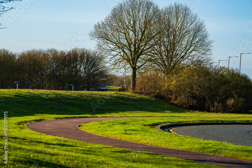 Winding pathway through green parkland near Stansted Airport. Curved walking trail with bare winter trees and grass slopes creates a serene landscape photo