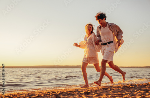 Smiling beautiful woman and her handsome boyfriend. Excited couple in casual clothes. Happy cheerful family. Female and man run at sunrise over sea beach outdoors. Run at seaside in summer day
