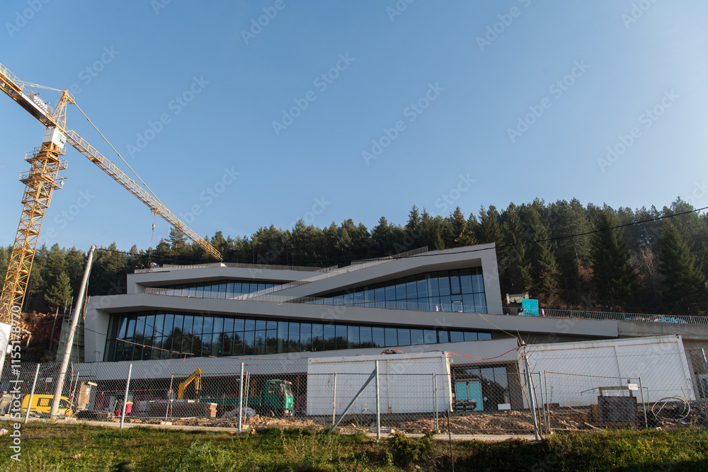 The exterior of a business building under construction is surrounded by trucks, cranes, and various construction materials, creating a bustling scene of an expansive industrial worksite in progress The exterior of a business building under construction is surrounded by trucks, cranes, and various construction materials, creating a bustling scene of an expansive industrial worksite in progress