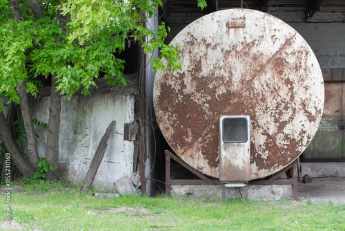 Old rusty tank sits in a grassy area beside a weathered building in the countryside photo