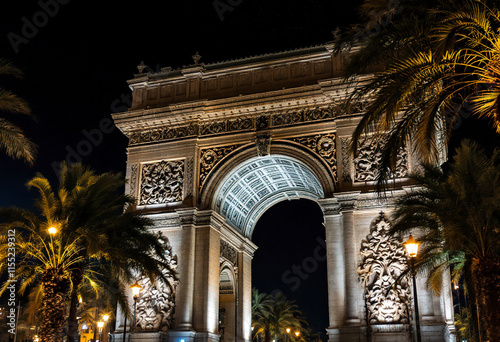 A large ornate stone arch with intricate architectural details, illuminated at night. The arch is surrounded by palm trees and appears to be the Arc de Triomf in Barcelona, Spain photo