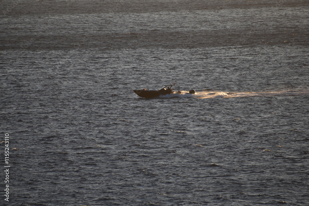 Fototapeta premium Speedboat gliding across the ocean at sunset leaving a trail of water behind The golden light reflects off the waves creating a dynamic and adventurous scene 