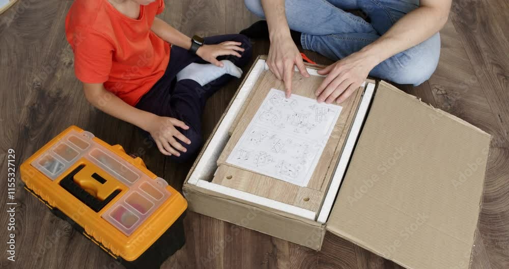 Father and son sit on the floor, unpacking furniture while studying the instruction manual. They share a moment of teamwork and learning, surrounded by boxes and tools