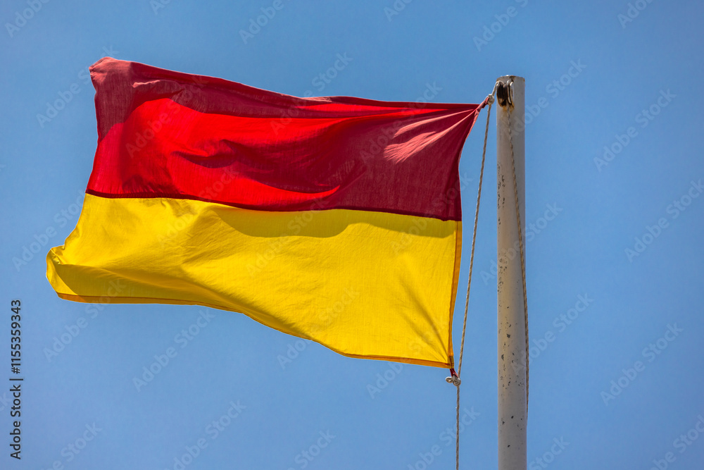 Red and yellow warning beach flag is under blue sky on a sunny day Red and yellow warning beach flag is under blue sky on a sunny day