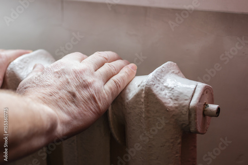 An elderly man warms his hands on the Central heating battery photo