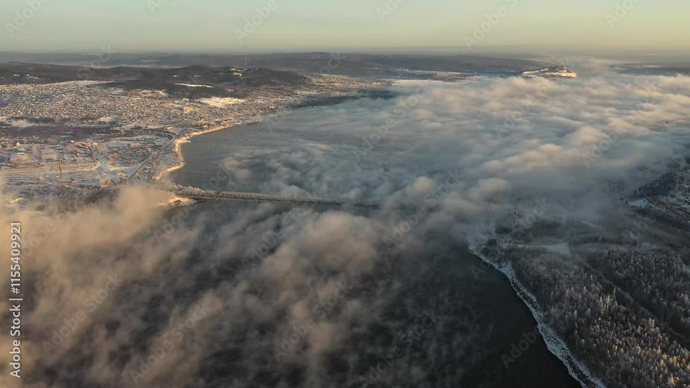 Drone flight at sunset over a lake with a dam in winter. The fog over the lake is illuminated by the setting sun. The dam is near the city. Drone flight at sunset over a lake with a dam in winter. The fog over the lake is illuminated by the setting sun. The dam is near the city.
