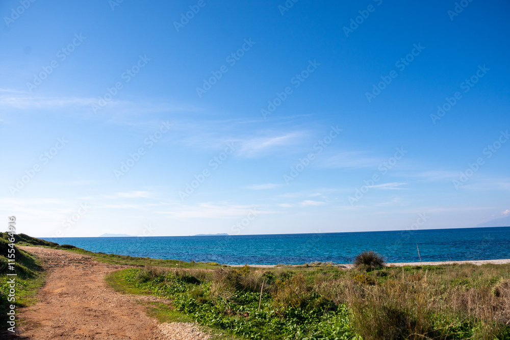 Serene coastal path leading to a tranquil blue sea under a clear sky. Serene coastal path leading to a tranquil blue sea under a clear sky.