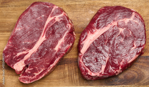 Photos Raw beef steak chuck eye roll on wooden board, top view