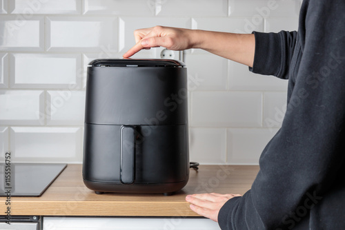 Woman at home using trendy kitchen gadget, deep fryer, selecting program on small convection oven on countertop for deep frying without oil, healthy way to cook fried food