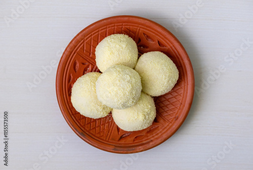 Tasty Kachagolla sweets served on a clay plate on a wooden background. Kanchagolla is a popular Bengali sweet delicacy known for its soft, spongy texture and subtle sweetness. Top view. photo