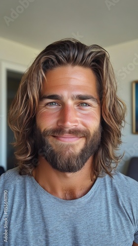 Handsome man with long hair and beard smiling in a modern indoor setting