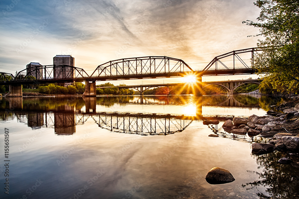Naklejka premium A bridge spans a river with a sunset in the background