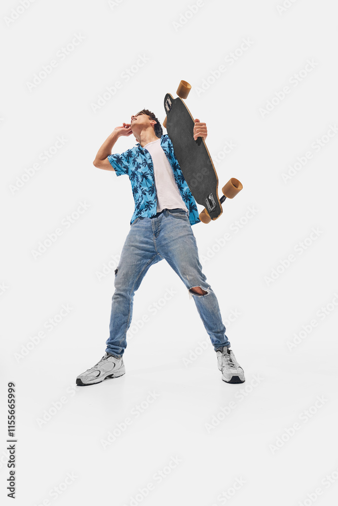 Wide angle photo. Skateboarder in blue patterned shirt, holding skateboard on shoulder, smiling confidently against white studio background. Concept of success, professional development, movement. Ad Wide angle photo. Skateboarder in blue patterned shirt, holding skateboard on shoulder, smiling confidently against white studio background. Concept of success, professional development, movement. Ad