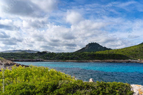  Cala Agulla, Mallorca, Spain, October 27, 2021 - Mountain peak rising above turquoise Mediterranean bay with pine forest