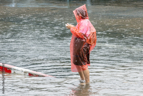 Canvas Print A woman in a raincoat stands in the middle of a large puddle and looks at her mo