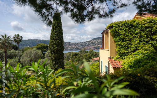 Saint-Jean-Cap-Ferrat, France - May 03, 2024: Mediterranean Villa Garden with Cypress Tree and Bay View Through Tropical Foliage