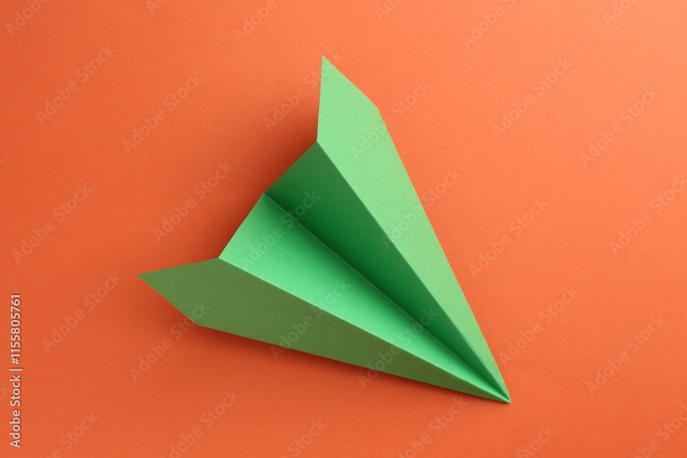 Fototapeta premium One handmade green paper plane on orange background, top view