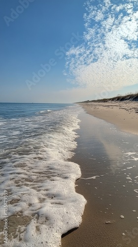 Serene coastal view under a clear blue sky with gentle waves and fluffy clouds