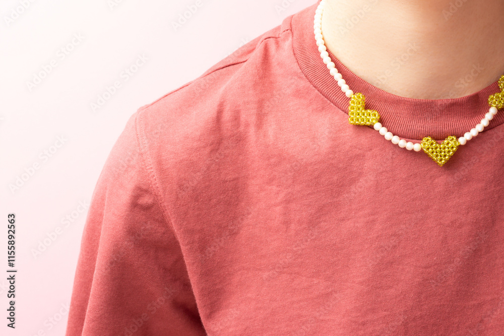 Handmade beads made from imitation pearls with green pendants in a heart shape on a woman in a t-shirt in front of pink background. Trendy accessory. Handmade beads made from imitation pearls with green pendants in a heart shape on a woman in a t-shirt in front of pink background. Trendy accessory.