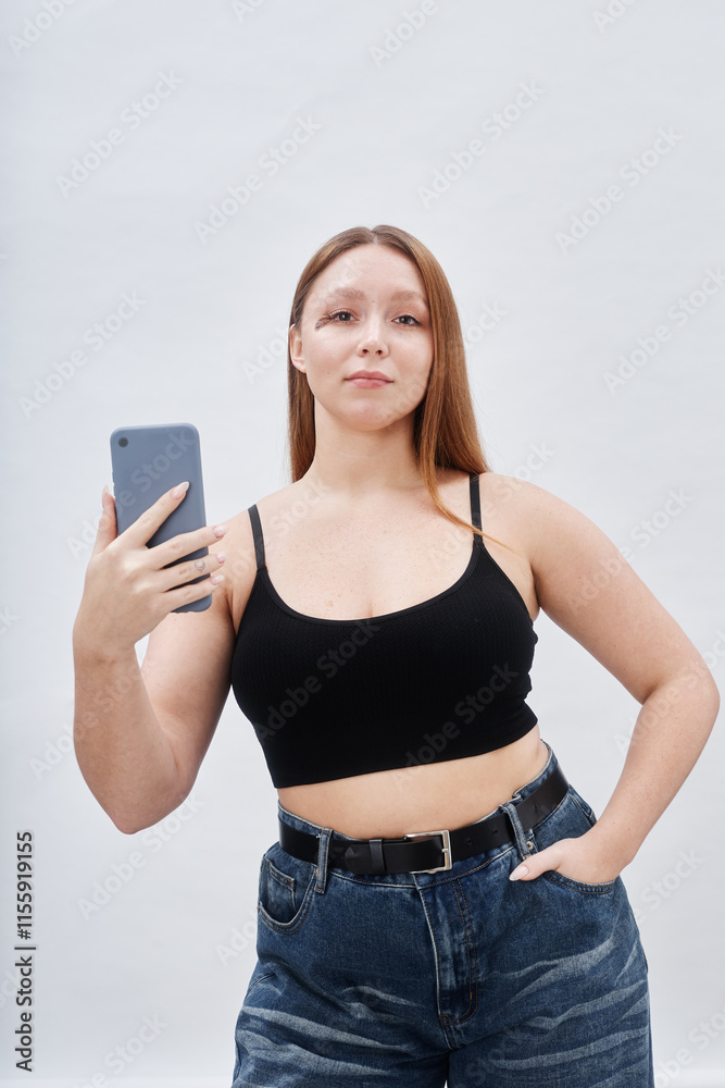 Medium full shot confident curvy woman with facial birthmark posing with hand in jeans pocket while snapping selfie and looking at camera against white backdrop in studio, copy space Medium full shot confident curvy woman with facial birthmark posing with hand in jeans pocket while snapping selfie and looking at camera against white backdrop in studio, copy space