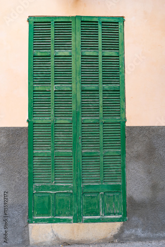 Capdepera, Mallorca, Spain 26.10.2021 Weathered green wooden shutters with horizontal louvered slats against beige wall