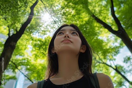 Young woman gazes upward in lush green park under sunlight filtering through ...