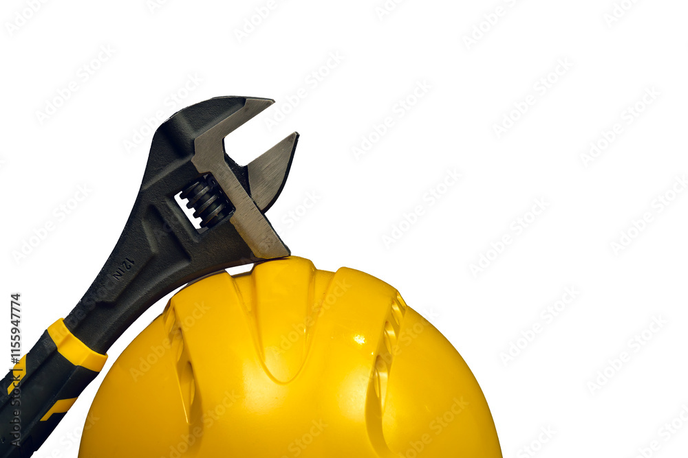 Adjustable wrench leaning on a yellow safety helmet on white background