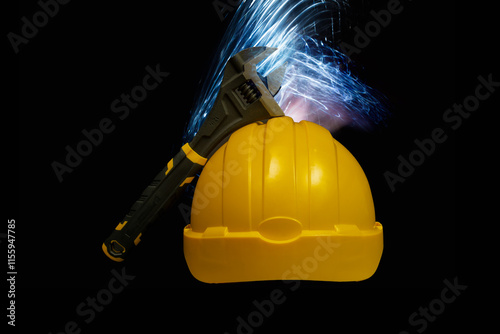 Obraz na płótnie Adjustable wrench leaning on yellow hard hat with blue sparks on black background w salonie
