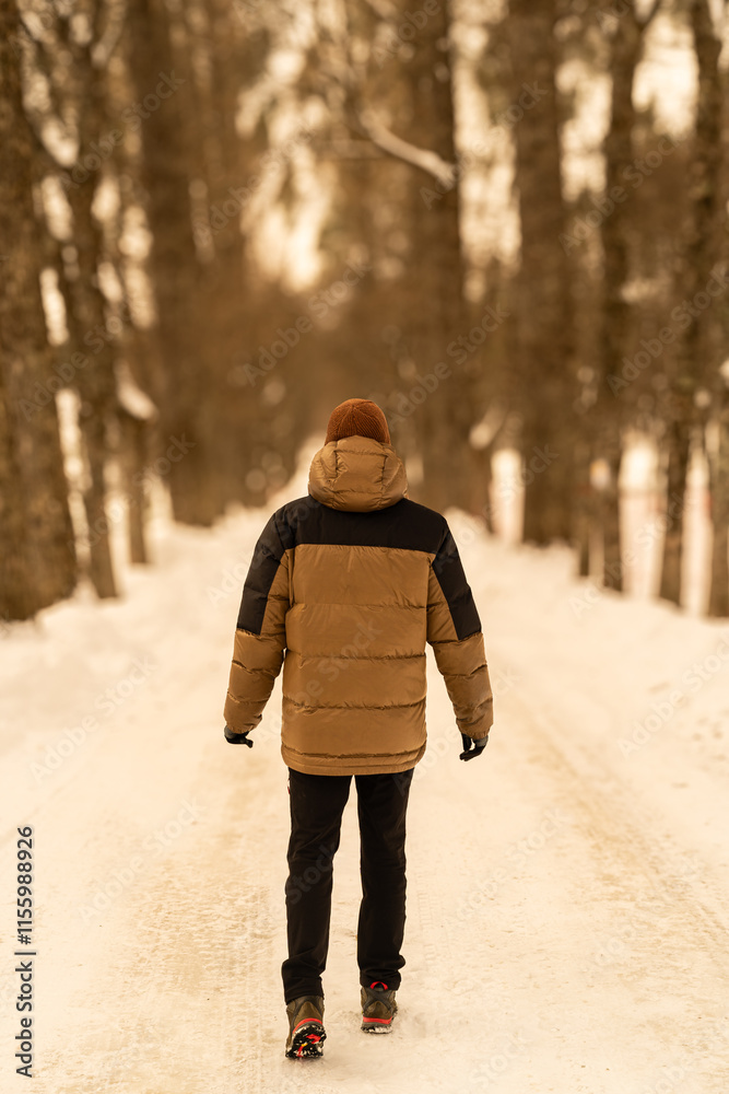 Man walking down snowy path wearing winter clothes and boots in a forest. Man walking away on snowy path wearing winter clothes in a forest Man walking down snowy path wearing winter clothes and boots in a forest. Man walking away on snowy path wearing winter clothes in a forest