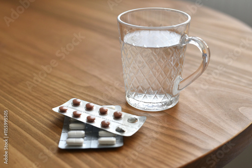 Glass of water and two blister packs of medicine tablets on wooden table