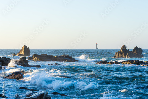 Scenic View of Phare de Nividic Lighthouse Amidst Rugged Coastal Rocks and Ocean Waves at Sunset in Ouessant, Brittany, France
