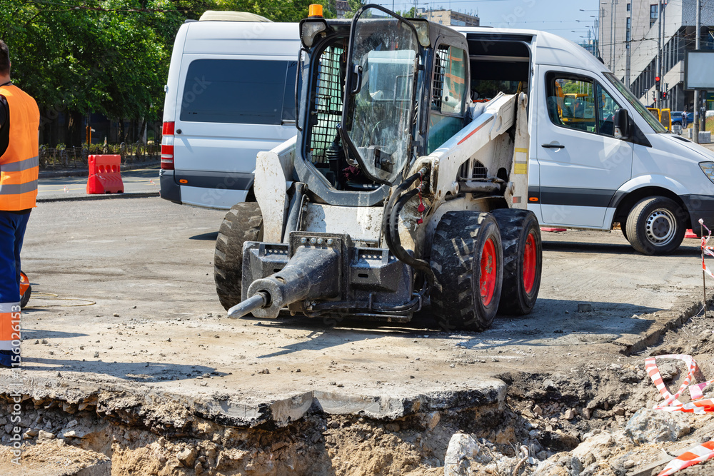 Construction vehicle operates on urban street to repair road damage during sunny day