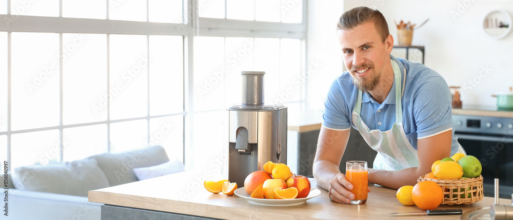 Young man with glass of fresh fruit juice near modern juicer in kitchen Young man with glass of fresh fruit juice near modern juicer in kitchen