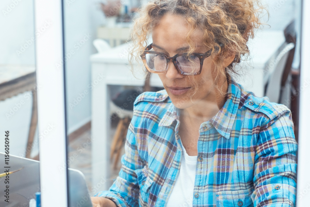© simona - Attractive middle-aged woman with curly hair sitting near a window, using her laptop for teleworking, browsing the internet, managing an online business, or handling stock market or cryptocurrency © simona - Attractive middle-aged woman with curly hair sitting near a window, using her laptop for teleworking, browsing the internet, managing an online business, or handling stock market or cryptocurrency