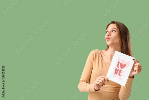 Beautiful young woman holding greeting card with word LOVE and heart on green background. Valentine's Day celebration