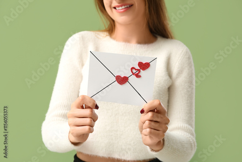 Beautiful young woman holding envelope with hearts on green background. Valentine's Day celebration